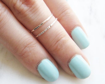 May include: Two thin silver rings stacked on a finger with light blue nail polish.