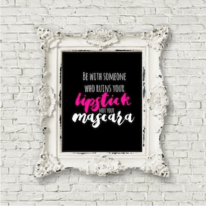 以下が含まれることがあります： 黒い背景に白い文字で「Be with someone who ruins your lipstick not your mascara」と書いてある、白い額縁に入ったプリント。ピンク色の文字で書かれています。