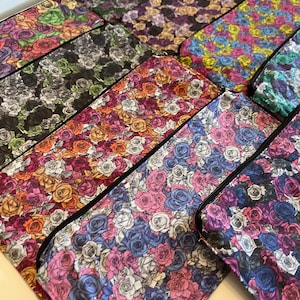 May include: A set of nine zippered pouches with a floral pattern featuring a variety of roses in different colors, including pink, blue, purple, yellow, and orange. The pouches have black zippers and are lined with black fabric.