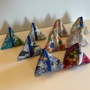 May include: Ten triangular zippered pouches with various colorful patterns and designs. The pouches are made of fabric and have a blue zipper. Some of the pouches have a small charm attached to the zipper.