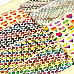 May include: A set of colorful zippered pouches with a variety of heart patterns. The pouches are made of a white fabric with a rainbow heart pattern, a black heart pattern, a pink heart pattern, a blue heart pattern, and a rainbow heart pattern with a white outline.