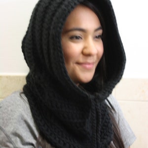 May include: A black crocheted hooded cowl with a long tie. The cowl is made of a thick yarn and has a loose, drapey fit.