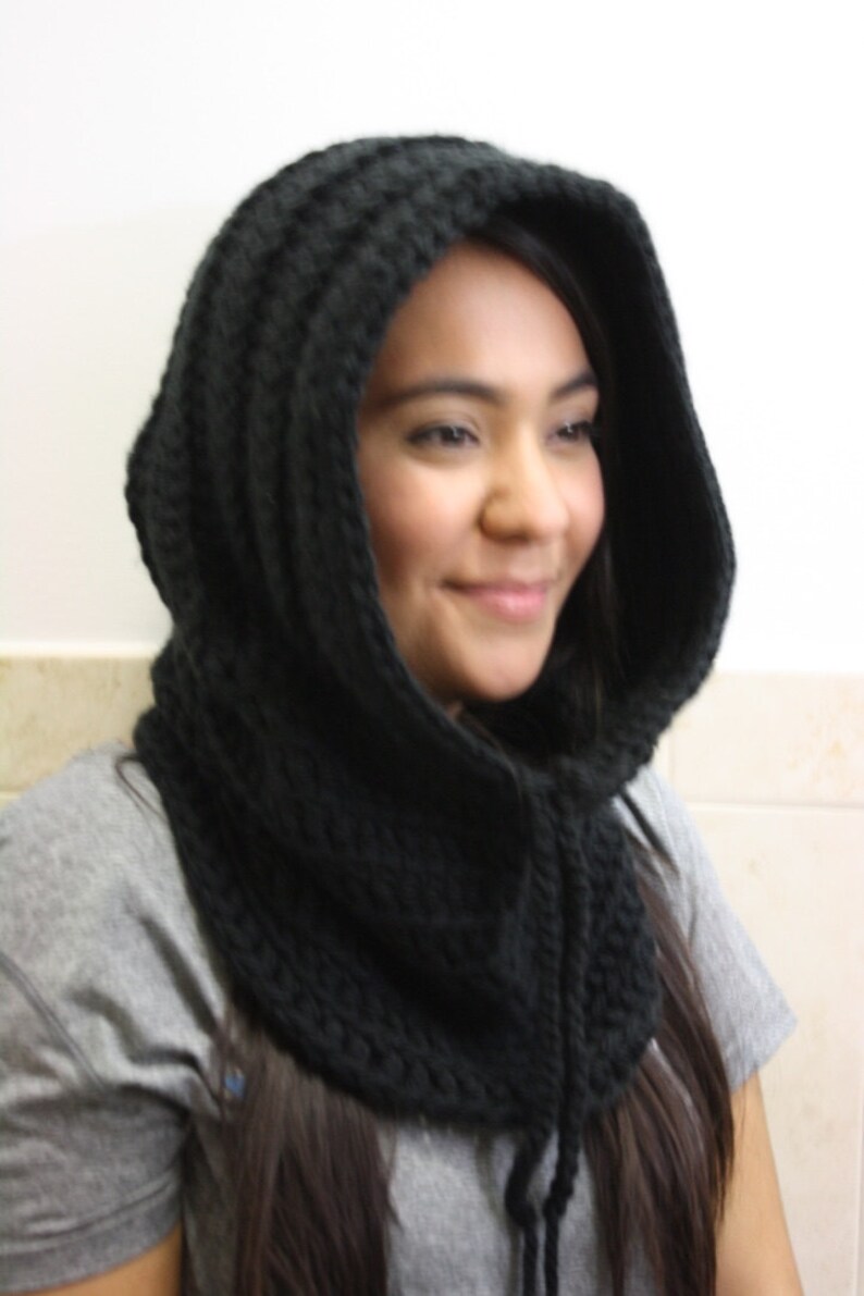 May include: A black crocheted hooded cowl with a long tie. The cowl is made of a thick yarn and has a loose, drapey fit.