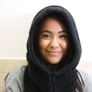 May include: A woman wearing a black knitted hooded scarf. The scarf is thick and has a cable knit pattern.