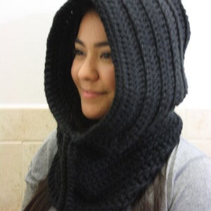 May include: A black crocheted hooded cowl with a long, dangling tie. The cowl is worn by a person with long, dark hair.