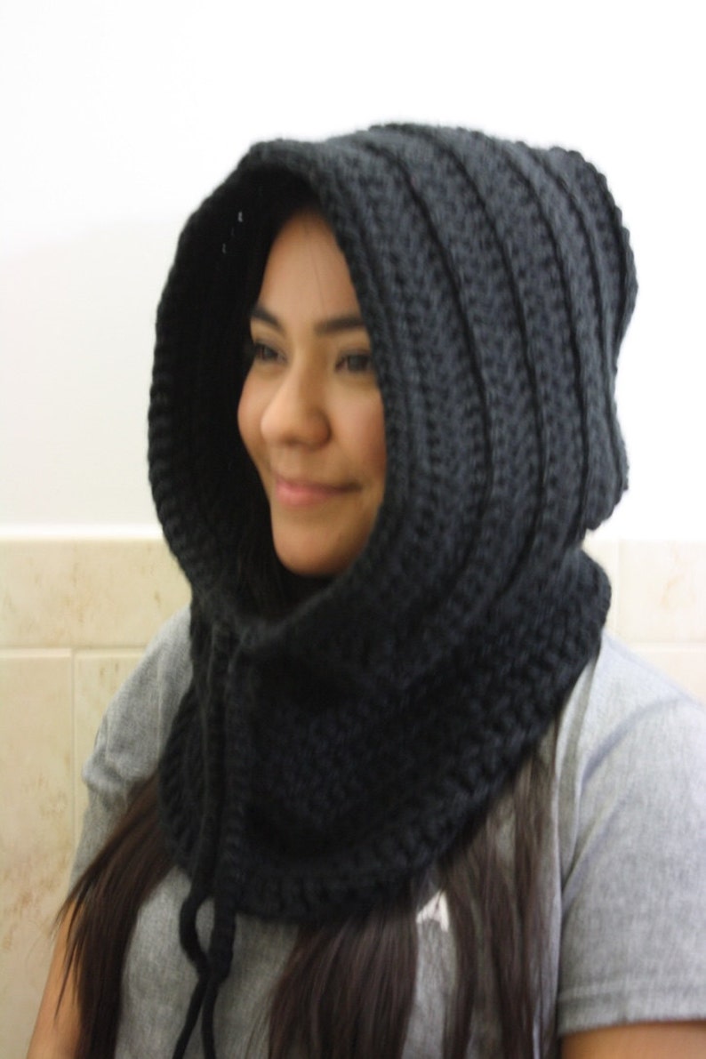 May include: A black crocheted hooded cowl with a long, dangling tie. The cowl is worn by a person with long, dark hair.