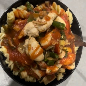 Puede incluir: Un bol negro lleno de pasta, pollo y verduras en una salsa de tomate roja.