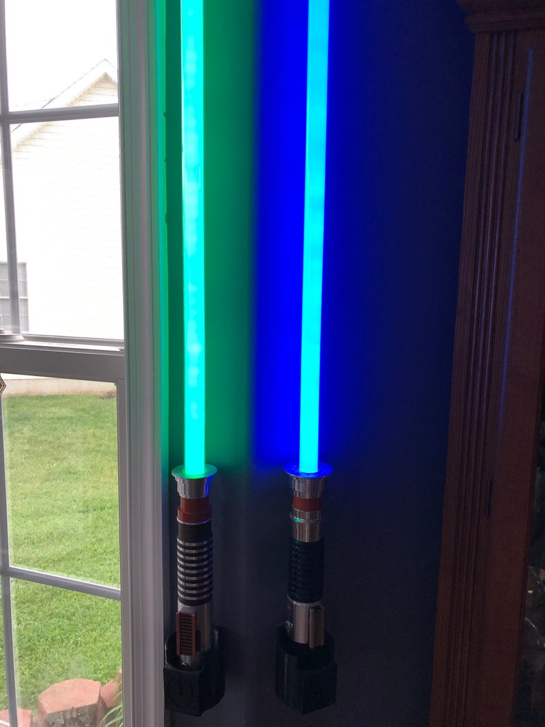 May include: Two light sabers mounted on a wall, one is green and the other is blue.
