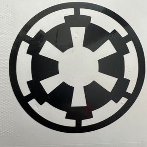 May include: A black and white sticker featuring the Star Wars Imperial symbol. The symbol is a circle with a black star in the center and a black border.