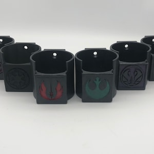 May include: Six black wall mounted cup holders with different Star Wars logos. The logos are in red, green, purple, and black.