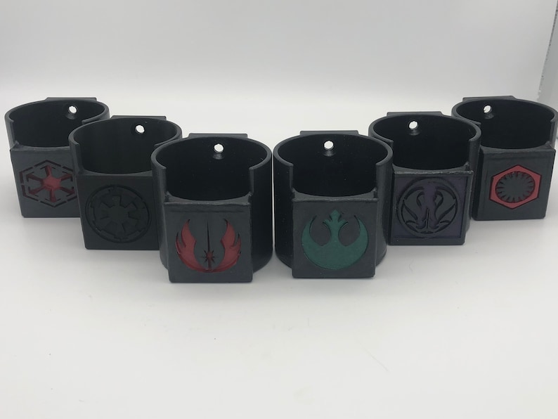 May include: Six black wall mounted cup holders with different Star Wars logos. The logos are in red, green, purple, and black.