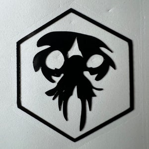 May include: Black and white illustration of a creature with large eyes and tentacles inside a black hexagonal frame.