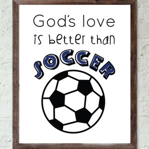 May include: A white framed print with the text "God's love is better than soccer" in black. A black and white soccer ball is centered below the text.