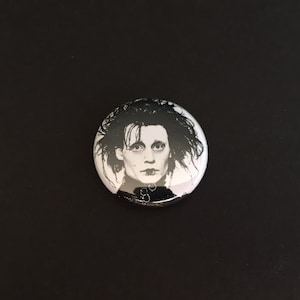 Può includere: Un bottone in bianco e nero con il ritratto di un uomo con i capelli scuri e un abito scuro. L'uomo guarda direttamente lo spettatore.