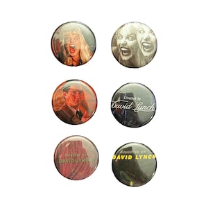 May include: A collection of six circular pin badges. The badges display images of people with expressions of shock and the text "Directed by David Lynch". The badges are in various colours, including black, white, and red.