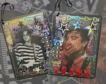 May include: Two rectangular clear plastic photo holders with black ball chains. The left holder features a person in a striped shirt and a purple character sticker. The right holder displays a person with red markings and the red text FRANK.