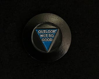 May include: A black and blue enamel pin with a triangle shape and the text "OUTLOOK NOT SO GOOD" inside.