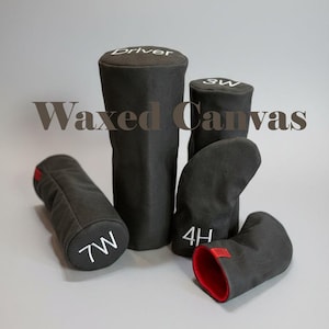 Könnte beinhalten: Eine Sammlung schwarzer Golfschlägerhauben mit weiß gesticktem Text, darunter "Driver", "3W", "4H" und "7W". Einige Hauben haben rote Akzente. Der Text "Waxed Canvas" ist im Bild zu sehen.