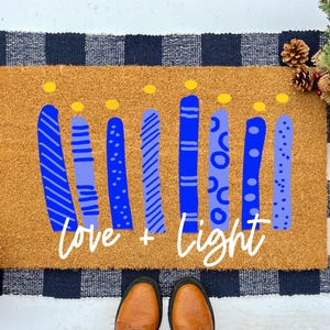 May include: A brown coir doormat with a blue and yellow design of candles and the text "love + light".