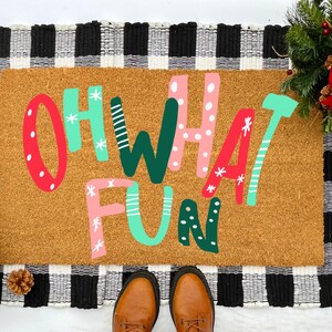 May include: A brown coir doormat with the words "Oh What Fun" written in colorful, stylized letters. The doormat is surrounded by a black and white checkered border.