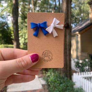 May include: Two small bows, one blue and one white, are displayed on a brown card with the text "The Green Porch".