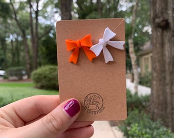 May include: Two small bow hair clips, one orange and one white, on a brown card with the text "The Green Porch".