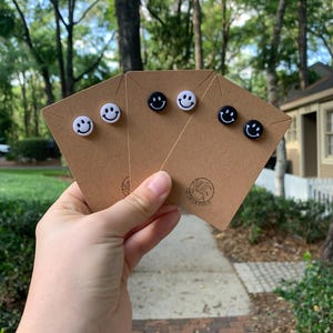 May include: A set of four smiley face earrings, two black and two white, displayed on a brown card with the text "The Green Porch".