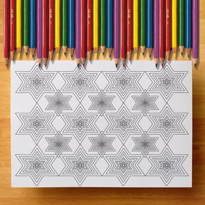 Pode incluir: L&aacute;pis de cor em v&aacute;rias cores, incluindo vermelho, amarelo, roxo e verde, s&atilde;o dispostos sobre uma folha de papel branca. A folha apresenta um padr&atilde;o repetitivo de formas de estrelas pretas, ideal para colorir.