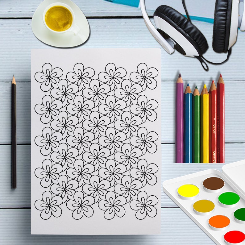 May include: A white sheet of paper with a black floral pattern, surrounded by colored pencils, a watercolor palette, a cup of coffee, a pencil, and headphones. The floral design is a repeating pattern of simple, five-petal flowers.