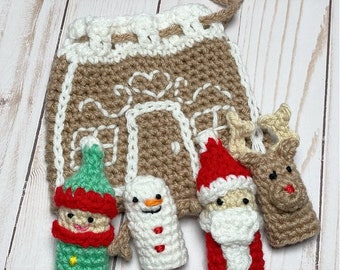 May include: A crocheted Christmas-themed gift bag with a gingerbread house design. The bag is tan with white accents and a white handle. Four crocheted finger puppets include an elf, snowman, Santa, and reindeer. The puppets are in various colors.