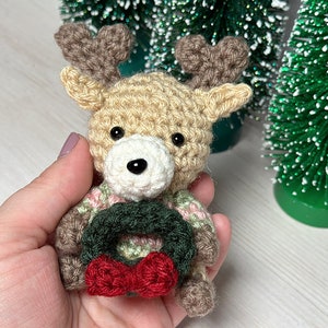K&ouml;nnte beinhalten: Ein geh&auml;keltes Rentier-Ornament mit einem braunen und wei&szlig;en K&ouml;rper, braunen Geweihen und einem gr&uuml;nen und roten Kranz um den Hals.