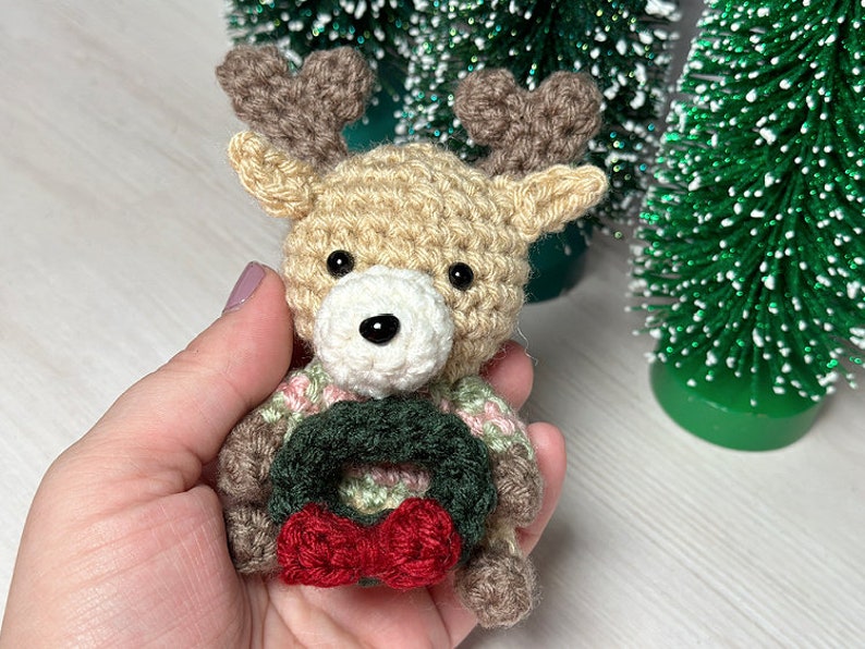 K&ouml;nnte beinhalten: Ein geh&auml;keltes Rentier-Ornament mit einem braunen und wei&szlig;en K&ouml;rper, braunen Geweihen und einem gr&uuml;nen und roten Kranz um den Hals.