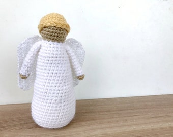 May include: A crocheted angel ornament with white wings and a light brown head. The angel is standing on a wooden surface.