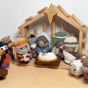 May include: A nativity scene featuring crocheted figures of the three wise men, a shepherd, a donkey, an angel, and a baby Jesus in a manger. The figures are arranged around a wooden stable.