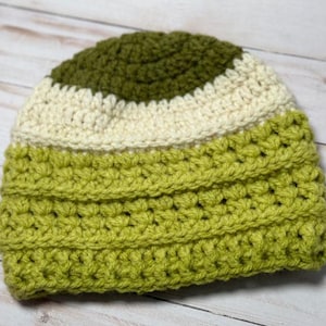 May include: A hand-crocheted beanie featuring three distinct horizontal color bands. The crown is a dark olive green, followed by a middle band of cream, and a wider base section in a vibrant lime green, all worked in a textured stitch pattern.