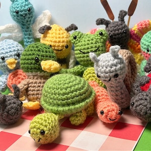 May include: A collection of crocheted animal plushies, including a ladybug, a frog, a snail, a turtle, a dragonfly, a bee, and a hummingbird. The plushies are all different colors and have cute faces.