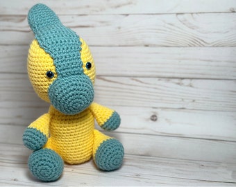 May include: A crocheted dinosaur toy with a yellow body and blue head and feet. The dinosaur has large blue eyes and a small, pointed nose.