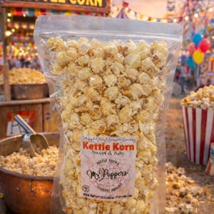 May include: A clear plastic bag filled with kettle corn, labeled "Kettle Korn Sweet & Salty" by Mr. Popper's. The background shows a carnival scene with a "KETTLE CORN" sign, a Ferris wheel, and colorful balloons.