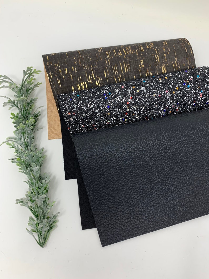 May include: Three sheets of fabric in different textures and colors. The top sheet is a brown cork fabric with gold flecks. The middle sheet is a black fabric with silver glitter and colorful flecks. The bottom sheet is a black faux leather fabric.