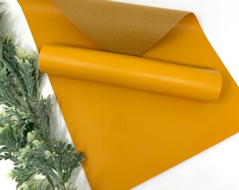 May include: A roll of mustard yellow faux leather with a brown suede backing. The leather is smooth and has a subtle texture.
