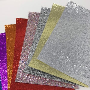 May include: A set of eight sheets of glitter paper in various colors, including purple, blue, orange, red, silver, and gold. The sheets are arranged in a fan shape, with the silver sheet at the top.