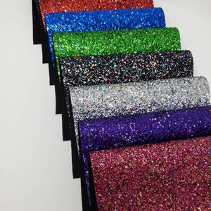 May include: A collection of eight sheets of glitter fabric in various colors, including black, red, blue, green, silver, purple, and pink. The fabric is textured and has a sparkly finish.