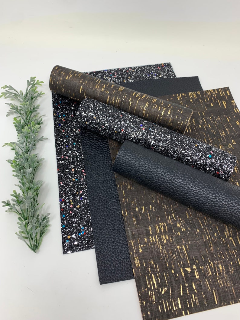 May include: A set of five fabric sheets in black and gold colors. The sheets have different textures, including glitter, cork, and faux leather.