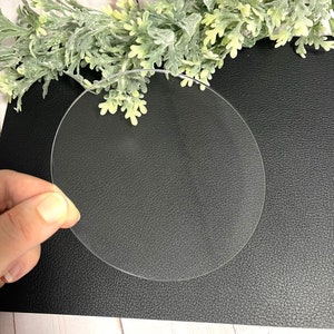 Puede incluir: Una pieza redonda de acr&iacute;lico transparente, de aproximadamente 15 cm de di&aacute;metro, sobre una superficie negra texturizada.