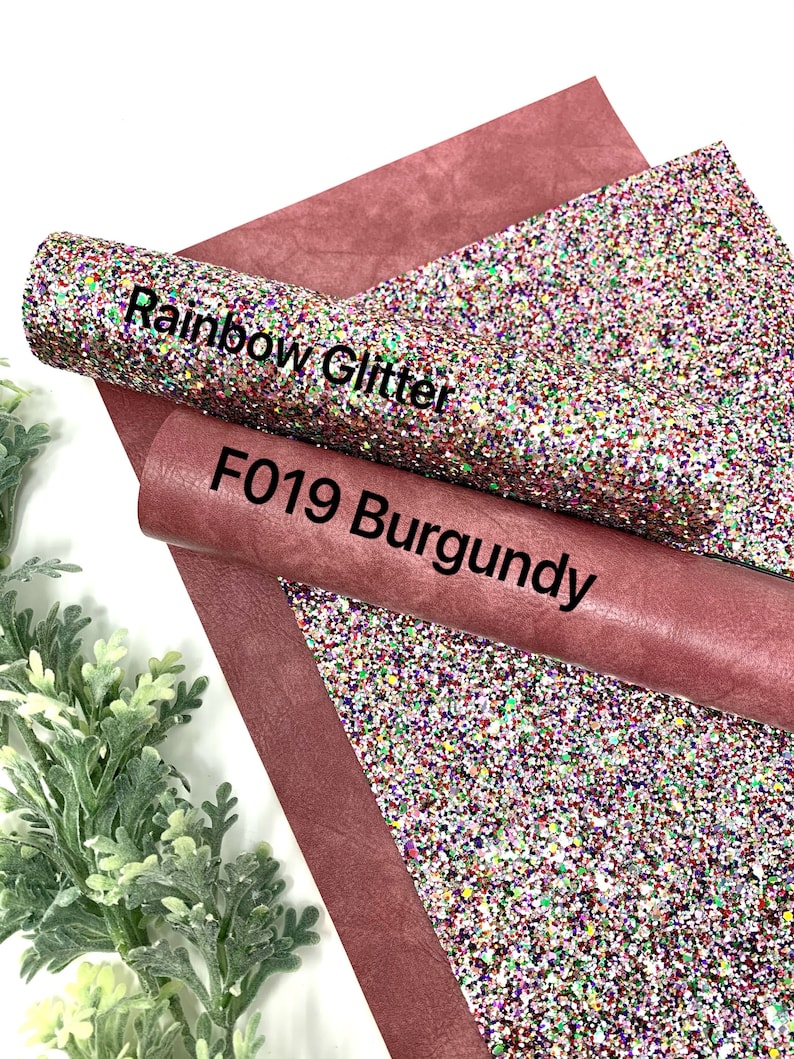 May include: A roll of burgundy faux leather with a roll of rainbow glitter fabric on top. The glitter fabric has a white base with multi-colored glitter. The text "Rainbow Glitter" and "F019 Burgundy" is printed on the fabric.
