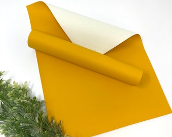 May include: A roll of yellow faux leather fabric with a white backing. The fabric is rolled up and the white backing is visible.
