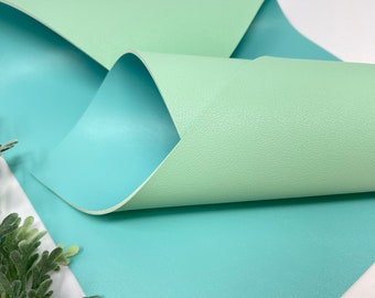 May include: A sheet of light green faux leather with a smooth, textured surface. The leather is folded in half, revealing a light blue side.
