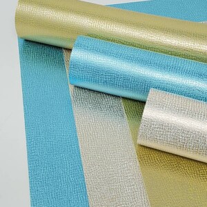 May include: Four rolls of metallic faux leather in gold, silver, and blue. The material has a textured, pebbled surface.