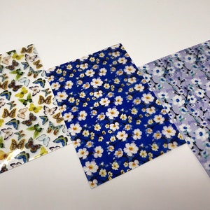 May include: Three sheets of decorative paper with floral and butterfly patterns. The first sheet features a white background with colorful butterflies. The second sheet has a blue background with white flowers. The third sheet has a light purple background with white flowers and black stems.