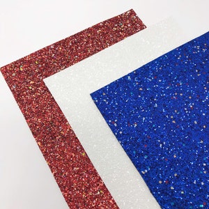 May include: Three sheets of glitter paper in red, white, and blue. The sheets are stacked on top of each other, with the red sheet on the bottom, the white sheet in the middle, and the blue sheet on top.